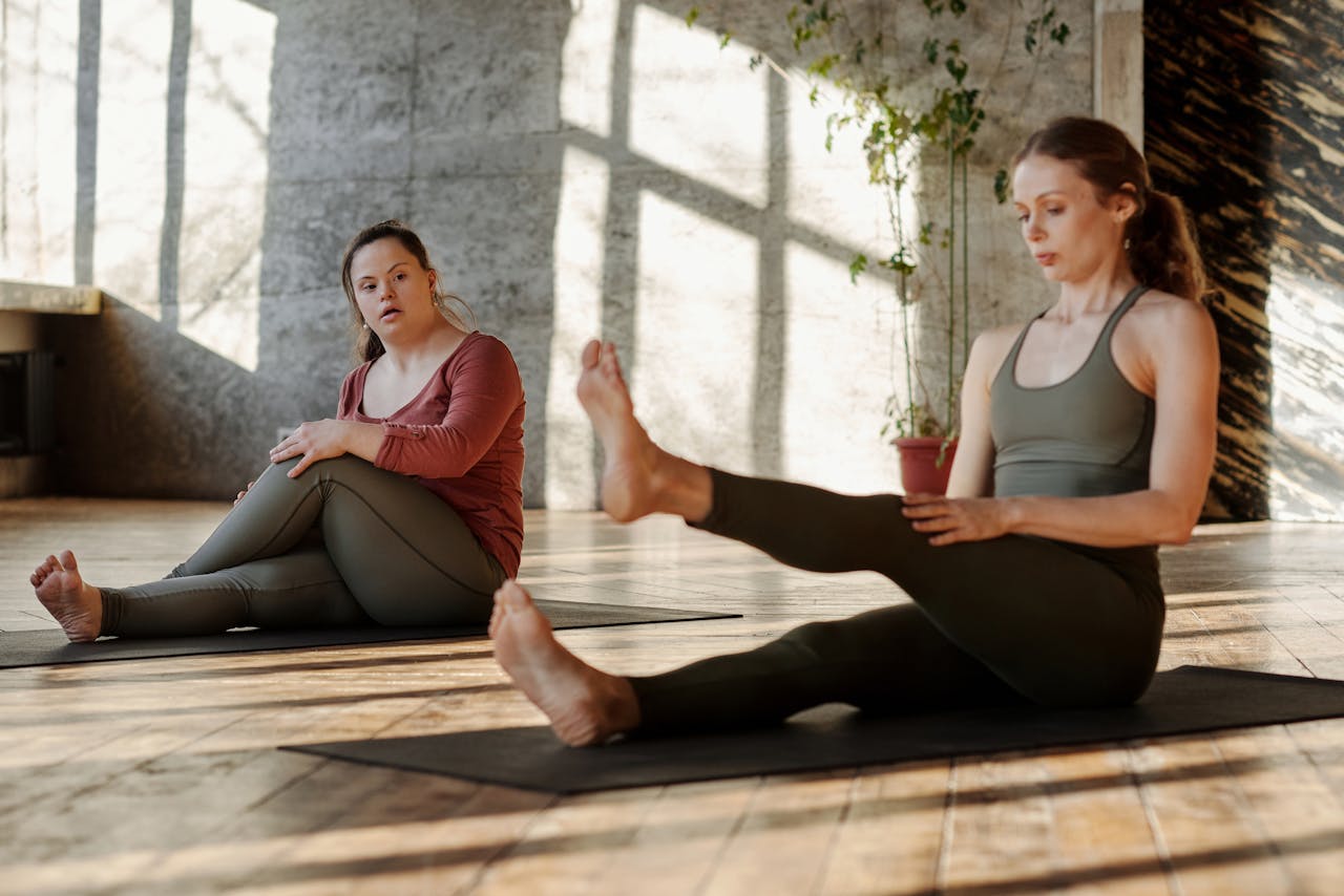 Two women engaging in inclusive yoga practice indoors, promoting wellness and flexibility.