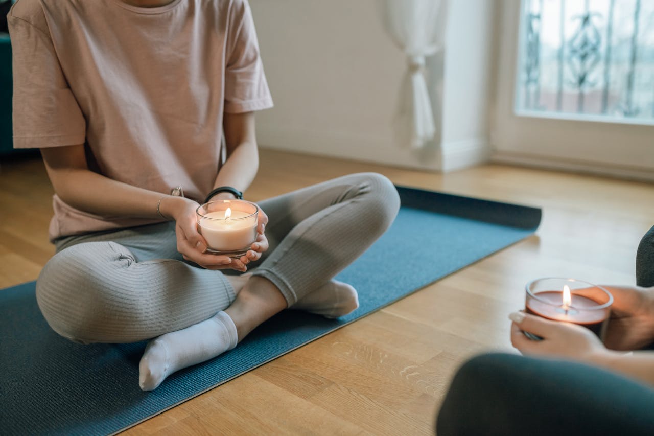 Woman holding a candle seated for meditation on yoga mat indoors.